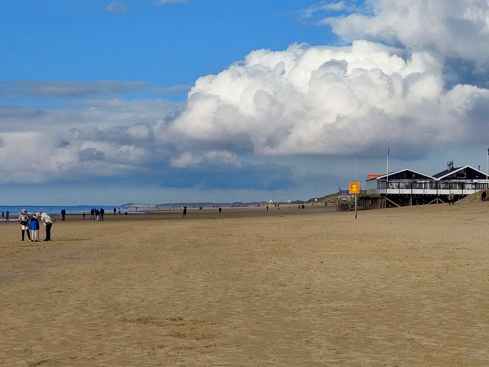 Breed zandstrand van Callantsoog met wandelaars en een strandpaviljoen onder een wolkenlucht